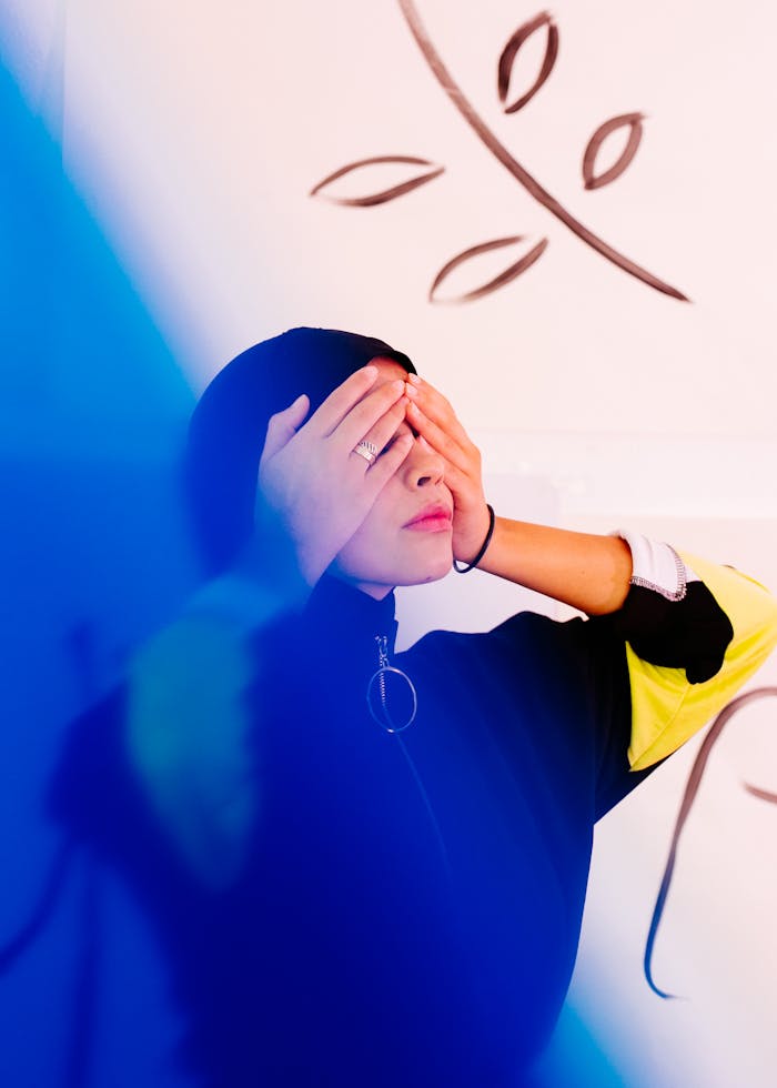 pexels photo 3819573 Young woman posing with hands over eyes, vibrant colors and artistic background.