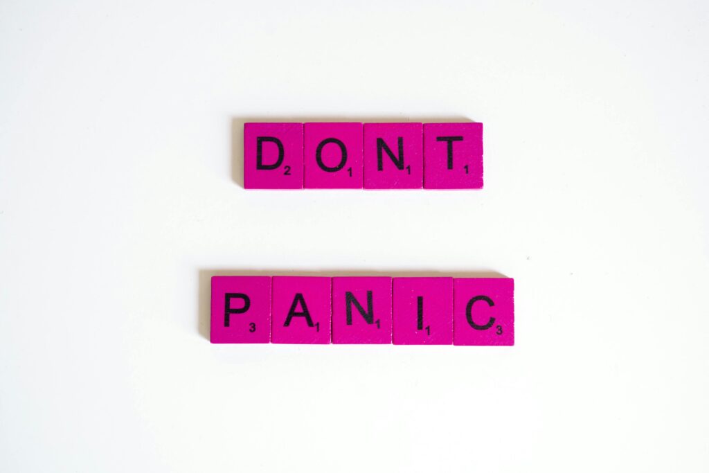 Self Help Pink Scrabble tiles spell out 'Don't Panic' on a white background.