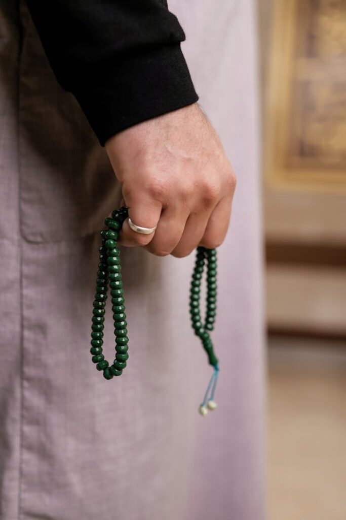 A close-up image of a hand holding green prayer beads, symbolizing meditation or spirituality.